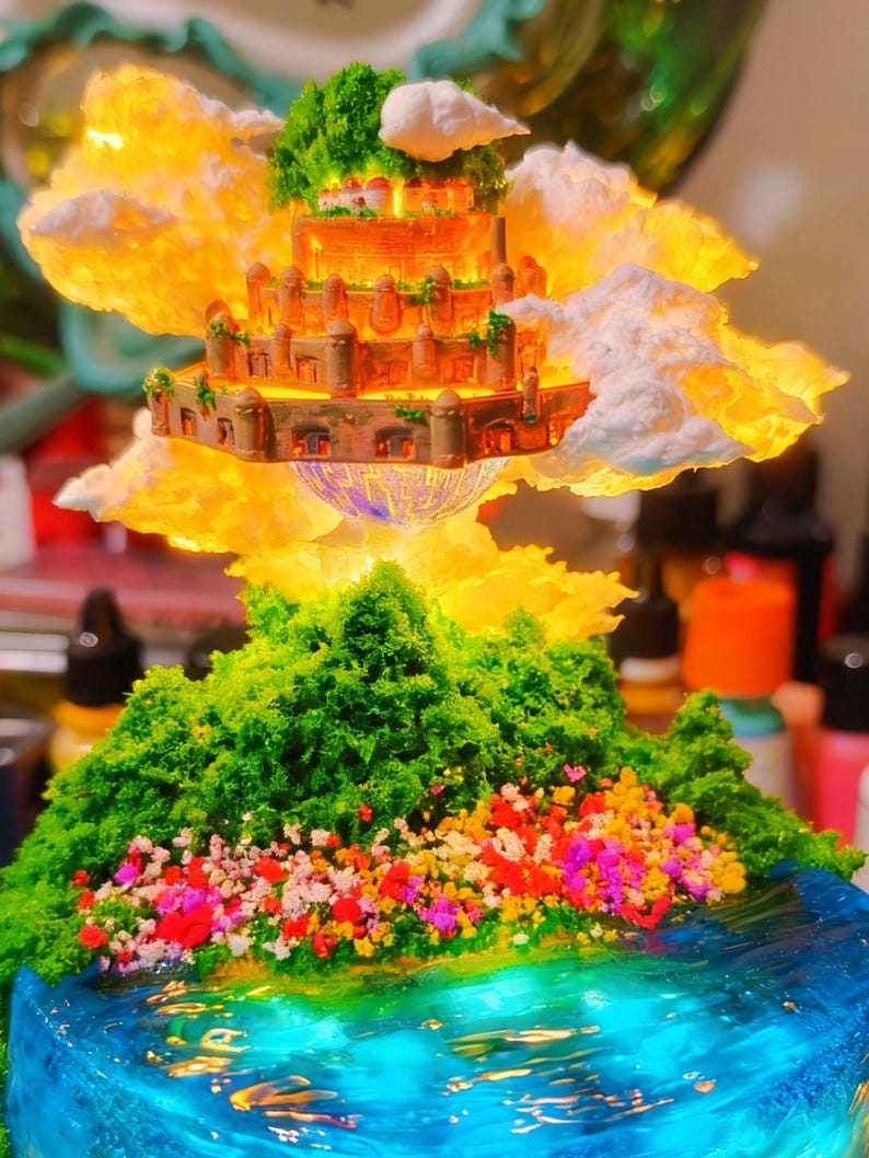 May include: A miniature fantasy landscape featuring a floating castle with detailed architecture, surrounded by fluffy clouds and illuminated by a warm glow. Below, a green, tree-covered island with colorful flowers sits above a blue, water-like base.