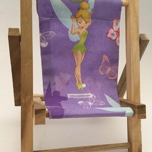 Puede incluir: Una peque&ntilde;a silla plegable de madera con un asiento de tela morado con un personaje de Campanilla y dise&ntilde;os de mariposas.