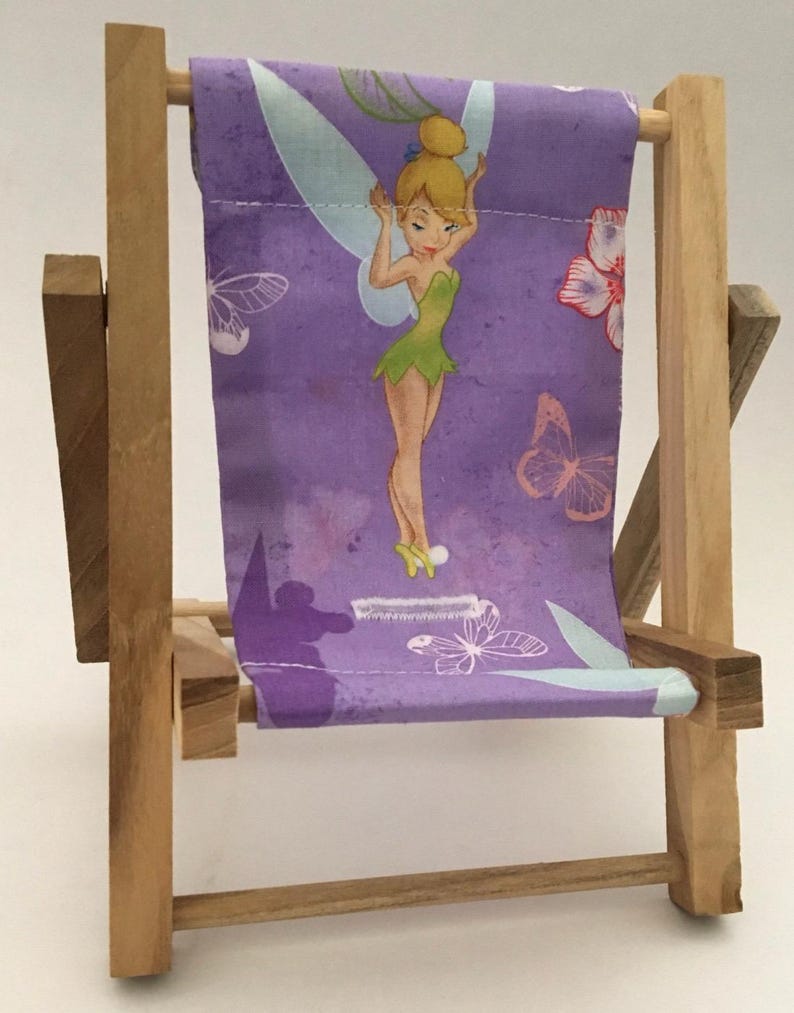 Puede incluir: Una peque&ntilde;a silla plegable de madera con un asiento de tela morado con un personaje de Campanilla y dise&ntilde;os de mariposas.