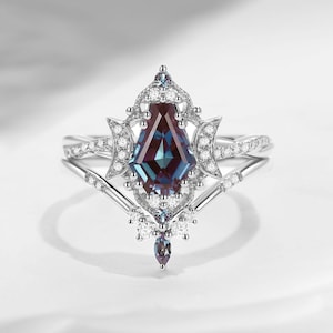 May include: A silver ring set featuring a large, multi-faceted, teal and purple gemstone. The ring is accented with small, clear gemstones and crescent moon shapes. The band is also adorned with small gemstones.