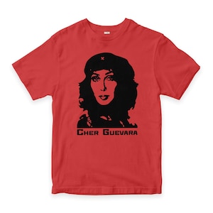 以下が含まれることがあります： 赤いTシャツ。黒いベレー帽をかぶった女性のシルエットと、下に「Cher Guevara」の文字がプリントされています。グラフィックは様式化された肖像画です。Tシャツは半袖でクルーネックです。