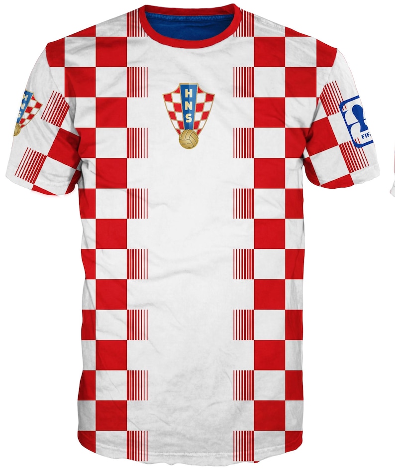 May include: A short-sleeved t-shirt featuring a red and white checkered pattern across the front and sleeves. The center chest displays the HNS crest with a soccer ball. A blue FIFA logo patch is visible on the right sleeve and a small crest on the left.