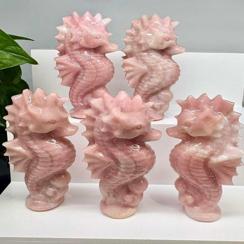 May include: A collection of six pink seahorse figurines. Each seahorse is carved from a translucent, light pink material, with detailed fins, tails, and spiky dorsal fins. The seahorses stand upright, showcasing their intricate design.