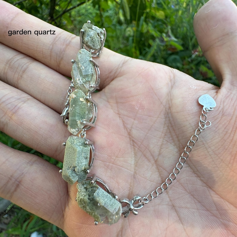 May include: A silver bracelet featuring rough-cut, light green garden quartz stones. The stones are held in place by silver settings and connected by a delicate chain. The text "garden quartz" is visible in the image.