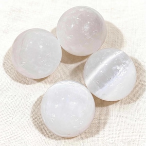 May include: Four white selenite spheres arranged in a square. The spheres have a smooth, polished surface and a translucent appearance. The spheres are a light, off-white color and appear to be made of a crystalline material.