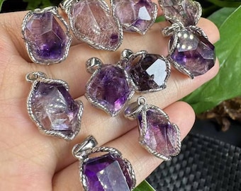 Op de afbeelding: Een verzameling amethist hangers met zilverkleurige, touwachtige frames. De amethist kristallen variëren in vorm en tint, variërend van diep paars tot doorschijnend lavendel. Elke hanger heeft een kleine lus voor een ketting.