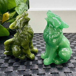 Puede incluir: Dos figuras de lobos talladas, una de color verde oscuro y otra de un tono verde más claro. Ambas están en posición de aullido, con la cabeza hacia atrás y la boca abierta. Las figuras están hechas de un material liso y pulido.
