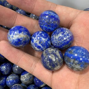 May include: A selection of polished lapis lazuli spheres. The deep blue orbs display lighter blue and grey marbling. The gemstones are smooth and reflect light, indicating a high polish. Each sphere is approximately 2.5 cm in diameter.