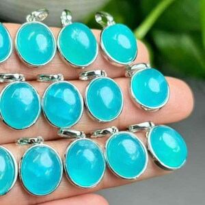 May include: Close-up of several oval pendants featuring a vibrant turquoise gemstone set in silver-coloured metal. The pendants are displayed closely, highlighting their polished surfaces and the reflective quality of the metal. The gemstones appear translucent.
