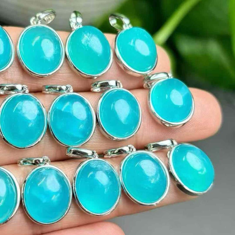 May include: Close-up of several oval pendants featuring a vibrant turquoise gemstone set in silver-coloured metal. The pendants are displayed closely, highlighting their polished surfaces and the reflective quality of the metal. The gemstones appear translucent.