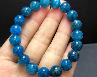 May include: A bracelet made of round, polished blue gemstone beads. The beads are a vibrant shade of blue, with variations in color and texture. The bracelet is strung together, forming a complete circle. The gemstones are approximately 1 cm in diameter.