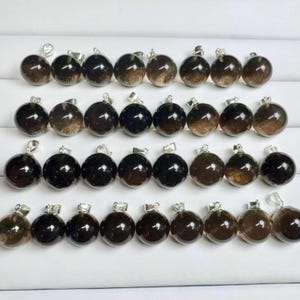May include: A selection of spherical, dark brown pendants with silver-coloured bails. The pendants have a polished, glossy finish and are arranged in neat rows. The colour varies from nearly black to a translucent brown.