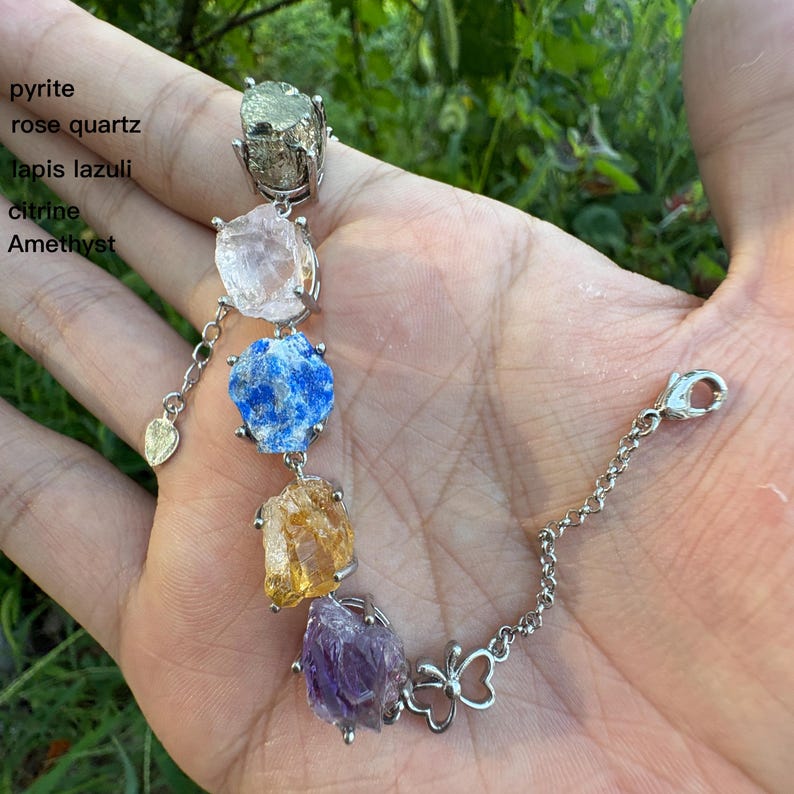 May include: A gemstone bracelet featuring pyrite, rose quartz, lapis lazuli, citrine, and amethyst. The bracelet has a silver chain and a butterfly charm. The gemstones are various colors, including gold, pink, blue, yellow, and purple.