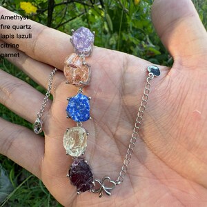 May include: A silver bracelet featuring a series of colorful gemstones: amethyst, fire quartz, lapis lazuli, citrine, and garnet. The gemstones are irregularly shaped and set in silver prongs. The bracelet has a delicate chain and a heart-shaped clasp.