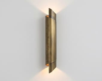 May include: A wall-mounted, cylindrical light fixture with a brass finish. The fixture has a unique, spiraling design with an open top and bottom, emitting a warm glow. The light is mounted on a white wall.
