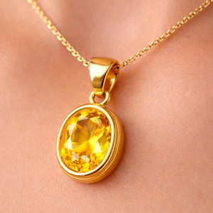 Peut inclure: Un collier doré avec un pendentif orné d'une grosse pierre jaune de forme ovale. La pierre est sertie dans un cadre doré et suspendue à une fine chaîne dorée. Le pendentif mesure environ 2,5 cm de long.