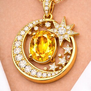 Op de afbeelding: Gouden hangerketting met een grote ovale gele edelsteen, omgeven door een maanvorm met diamanten. Een ster en kleinere diamanten sterren maken het ontwerp compleet. De ketting heeft een gouden ketting.