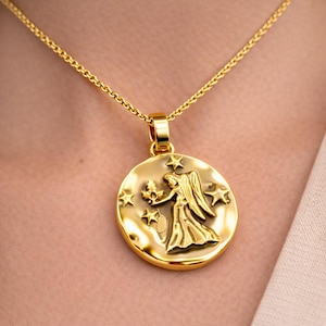 May include: A gold pendant necklace with a Virgo zodiac design. The circular pendant shows a winged figure with a bouquet, encircled by stars. The necklace has a fine chain.