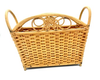 May include: A rectangular wicker basket with two curved handles and a decorative knot detail. The basket is woven from light brown wicker and has a sturdy, open design. Ideal for storage or display, it measures approximately 30cm in length.