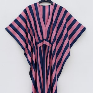 May include: A floor-length kaftan dress featuring vertical stripes in alternating shades of dusty pink and navy blue. The garment has a deep V-neckline, wide kimono-style sleeves, and a fitted waist panel that creates a draped, flowing silhouette.