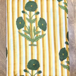 May include: Folded fabric with a yellow and white striped background. The fabric features a repeating pattern of green floral designs with detailed leaves and flower heads. The overall aesthetic is bright and decorative.