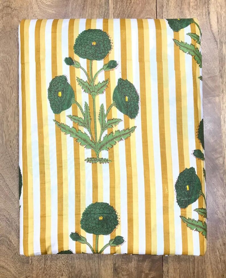 May include: Folded fabric with a yellow and white striped background. The fabric features a repeating pattern of green floral designs with detailed leaves and flower heads. The overall aesthetic is bright and decorative.