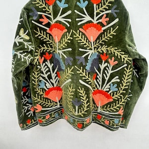 May include: A dark green velvet jacket with colorful floral embroidery. The embroidery features orange, blue, and white flowers with gold and green leaves. The jacket has a high collar and a decorative border along the bottom.
