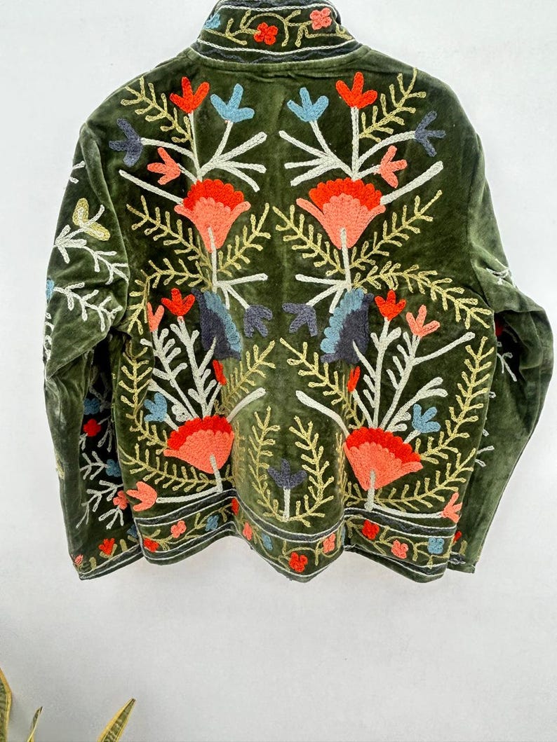 May include: A dark green velvet jacket with colorful floral embroidery. The embroidery features orange, blue, and white flowers with gold and green leaves. The jacket has a high collar and a decorative border along the bottom.