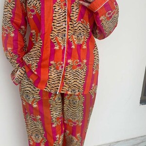 May include: A two-piece pajama set in a vibrant orange and pink striped pattern, featuring a repeating tiger print. The set includes a button-down shirt with white trim and matching trousers. The pajamas are made of a soft, comfortable material.