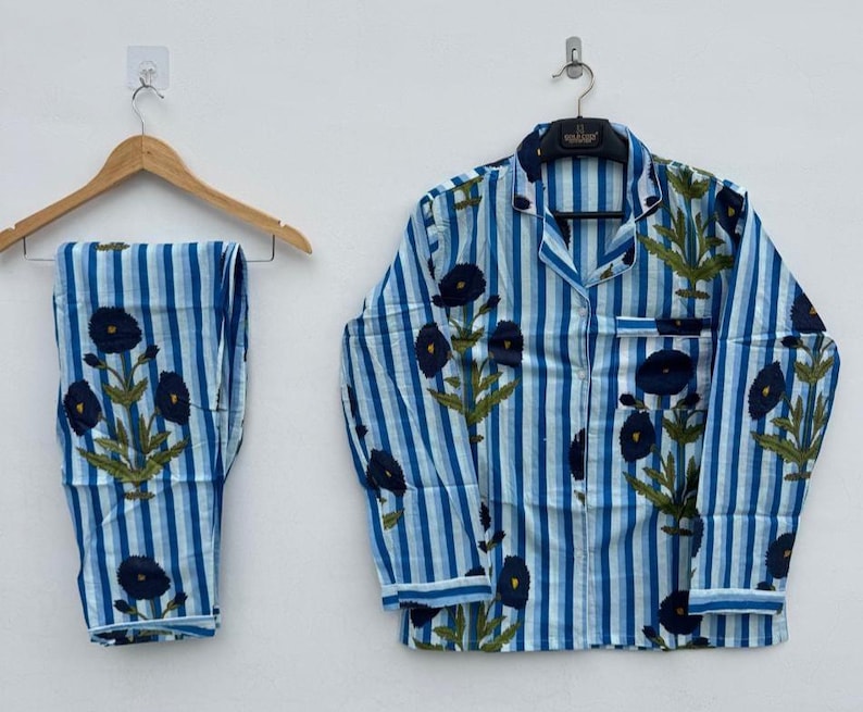 May include: Blue and white striped pajama set with a floral pattern. The set includes a button-down shirt with a chest pocket and matching pants. The floral design features dark blue flowers and green leaves.