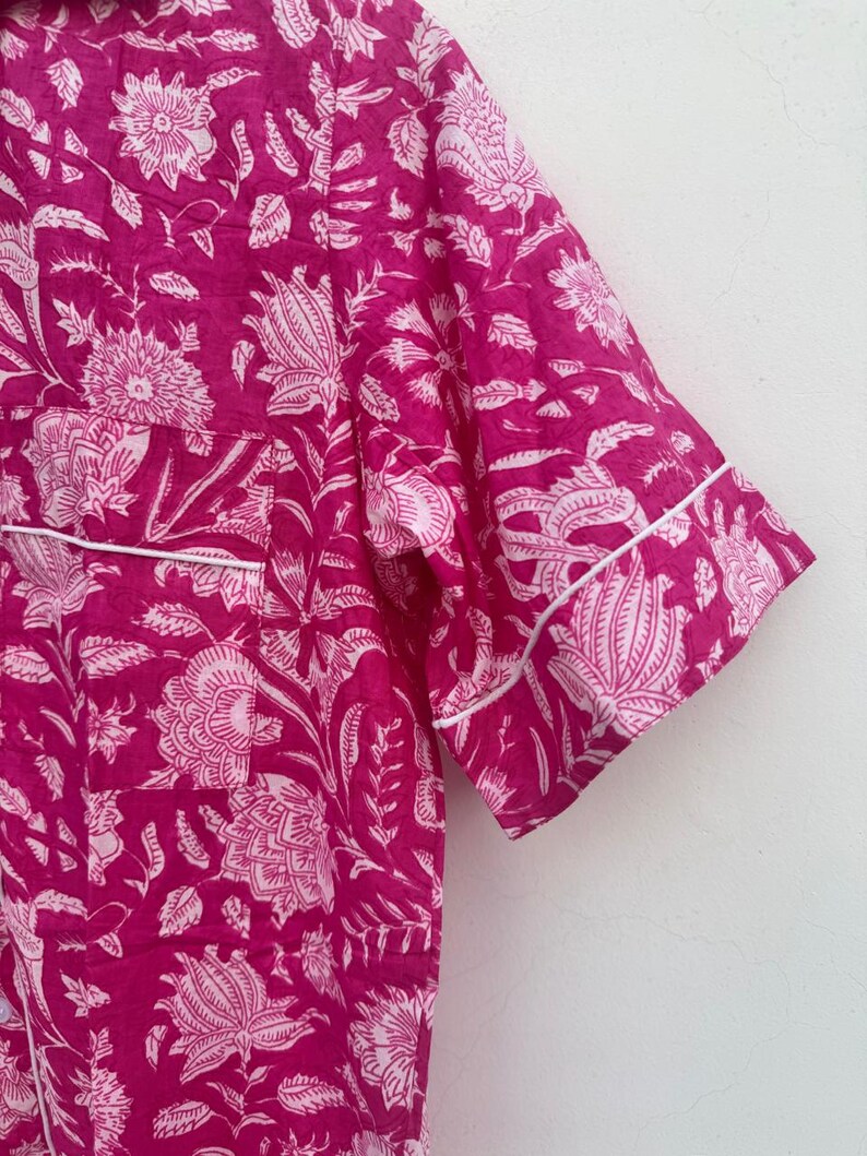 May include: A close-up of a magenta pajama top with a white floral pattern. The short-sleeved top has white piping along the edges. The fabric is a soft, lightweight material, perfect for sleepwear.