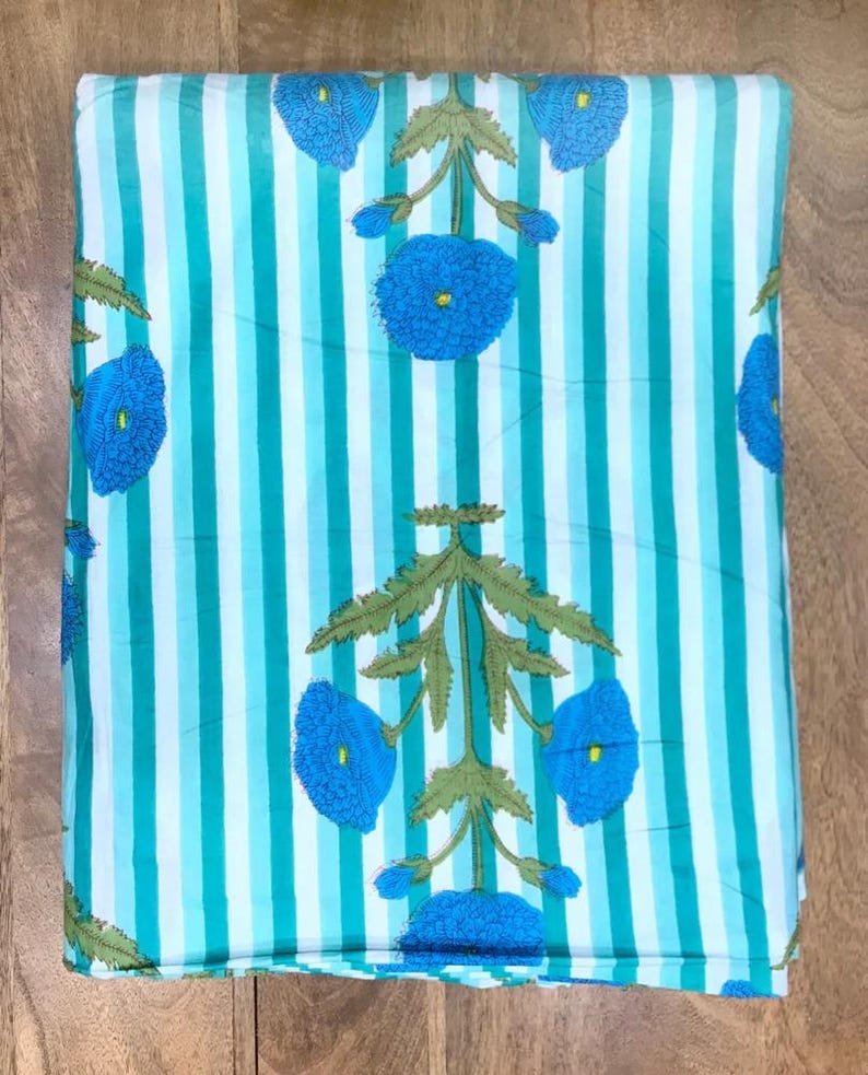 May include: Folded fabric with a striped pattern in shades of turquoise and white. The fabric features a repeating floral design in blue and green, with stylized flowers and foliage. The fabric is folded neatly, showing the pattern clearly.