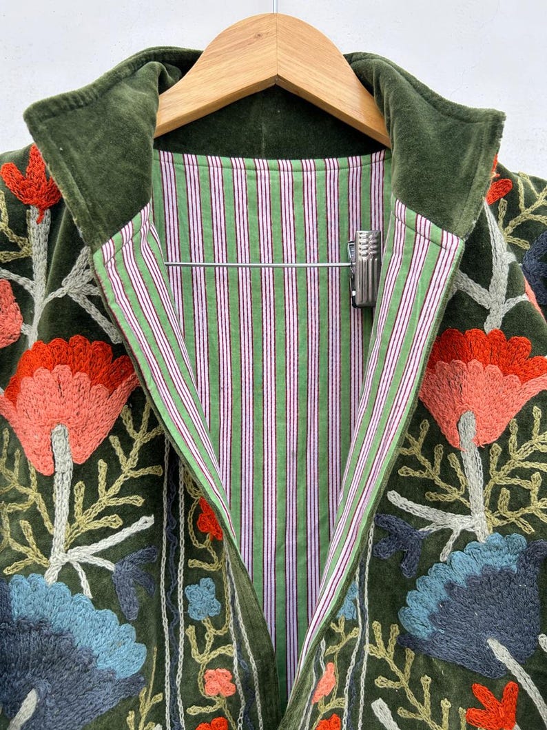 May include: A dark green velvet jacket with floral embroidery in shades of orange, blue, and green. The jacket features a striped lining in green and white with pink accents and a green velvet collar.