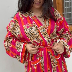 May include: A vibrant, long-sleeved robe with a tiger stripe pattern in shades of pink, orange, and brown. The robe has a white trim and a matching belt. The garment is made of a soft, lightweight fabric.