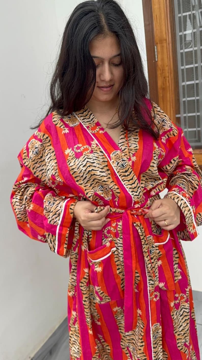 May include: A vibrant, long-sleeved robe with a tiger stripe pattern in shades of pink, orange, and brown. The robe has a white trim and a matching belt. The garment is made of a soft, lightweight fabric.