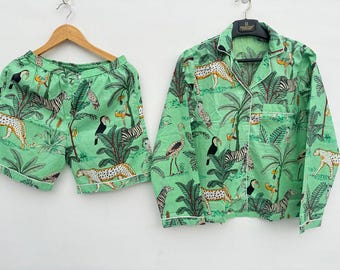 Peut inclure: Un ensemble de pyjama vert clair avec un imprimé jungle représentant des zèbres, des léopards, des toucans et des palmiers. L'ensemble comprend une chemise boutonnée et un short, tous deux bordés d'un passepoil blanc. Le tissu semble léger.