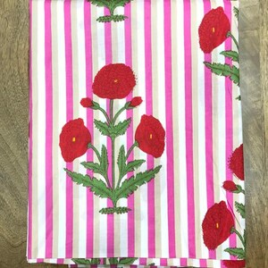 May include: Folded fabric with a pink and white striped pattern. Large red poppy flower designs with green leaves are printed on the fabric. The fabric is folded neatly, showcasing the floral and striped design.