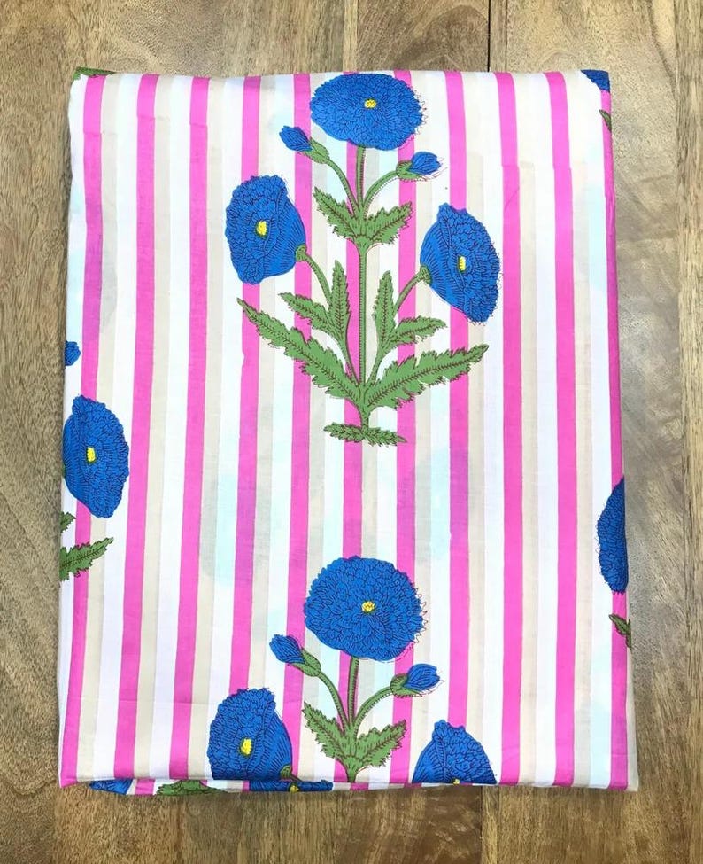 May include: Folded fabric with a pink and white striped background. The fabric features a repeating pattern of blue flowers with green leaves and stems. The flowers have yellow centers.