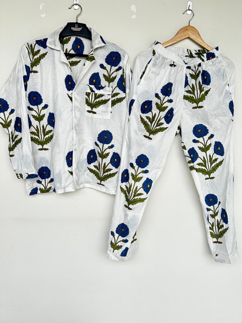 May include: White pajama set with a blue floral pattern. The set includes a button-down shirt with a chest pocket and pants with an elastic waistband. The floral design features blue flowers and green leaves.