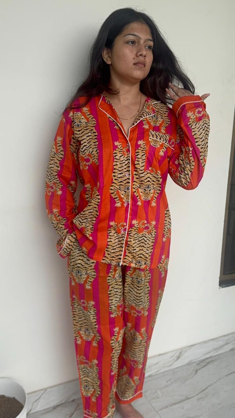 May include: An eye-catching orange pajama set featuring a tiger stripe design. The set comprises a button-down shirt and matching trousers, both trimmed with white. The pajamas are made from a soft, lightweight material.