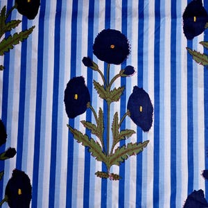 May include: Textile with a blue and white striped background. Dark blue floral pattern with yellow centers and green leaves. The design is repeated across the fabric, creating a visually appealing pattern.
