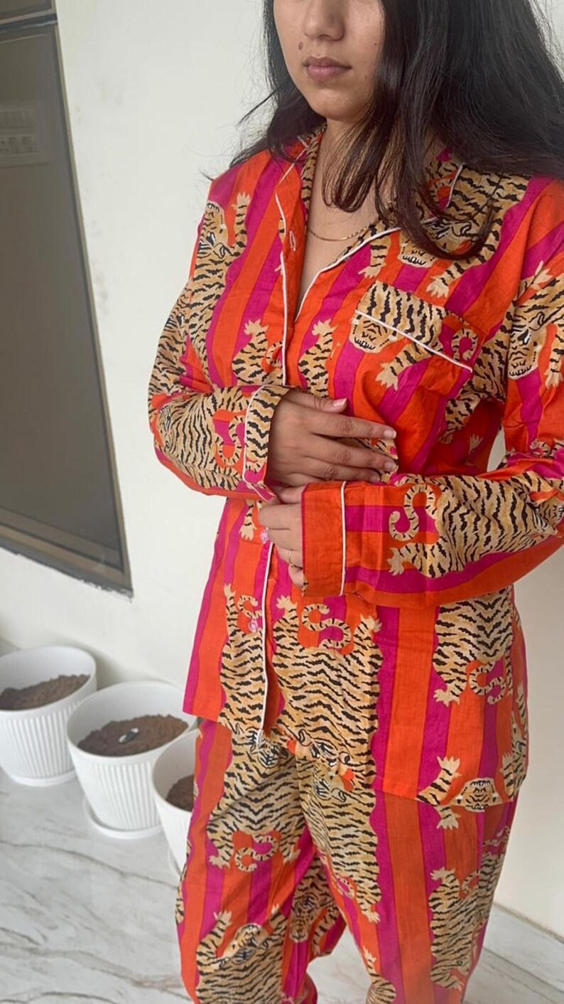 May include: A two-piece pyjama set in orange and pink stripes, featuring a tiger print. The long-sleeved top has white trim and a breast pocket. The matching trousers complete the sleepwear set.