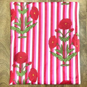May include: Folded fabric with a vertical striped pattern in red, pink, and white. The fabric is decorated with embroidered red poppy flowers and green leaves. The overall design is a floral and striped pattern.