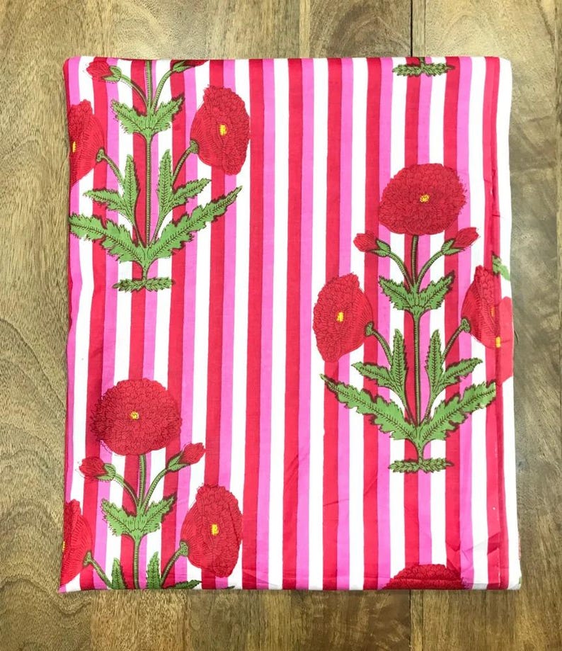 May include: Folded fabric with a vertical striped pattern in red, pink, and white. The fabric is decorated with embroidered red poppy flowers and green leaves. The overall design is a floral and striped pattern.