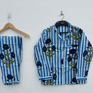 May include: Blue and white striped pajama set with a floral pattern. The set includes a button-down shirt and matching pants. The shirt and pants are adorned with dark blue flowers and green leaves.