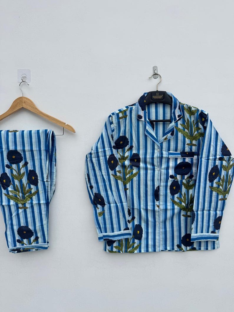 May include: Blue and white striped pajama set with a floral pattern. The set includes a button-down shirt and matching pants. The shirt and pants are adorned with dark blue flowers and green leaves.