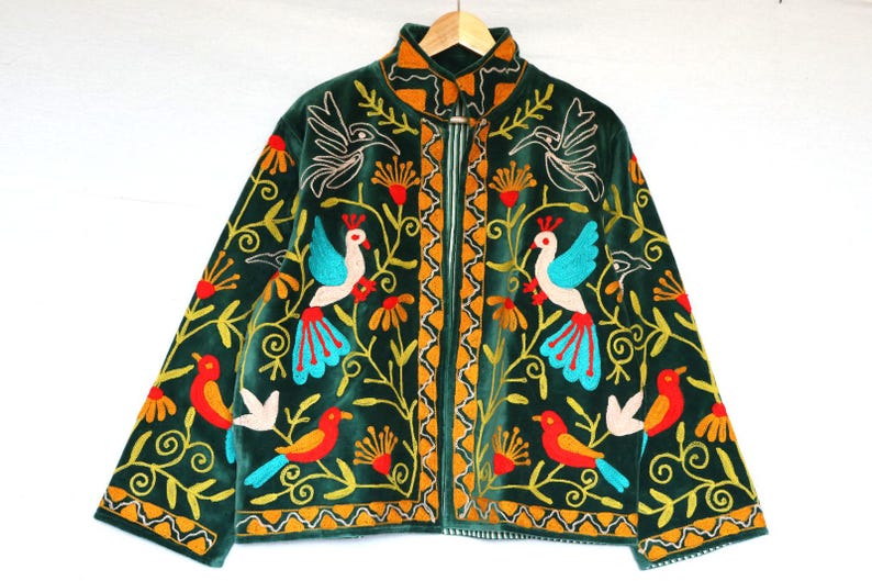 May include: A dark green velvet jacket with colorful embroidered birds and floral patterns. The jacket has a high collar, a zipper closure, and long sleeves. The embroidery features birds with blue, red, and yellow accents, and the jacket is approximately 30 inches long.