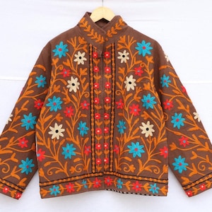 May include: Brown jacket with floral embroidery in orange, red, blue, and white. The jacket has a mandarin collar and long sleeves. The floral design is symmetrical and covers the front and sleeves.