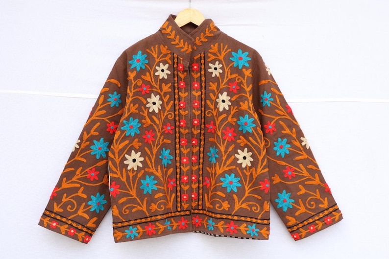 May include: Brown jacket with floral embroidery in orange, red, blue, and white. The jacket has a mandarin collar and long sleeves. The floral design is symmetrical and covers the front and sleeves.
