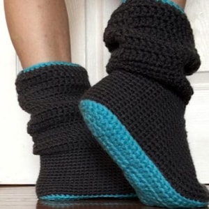 Puede incluir: Un par de botas de pantuflas de ganchillo gris oscuro con un ribete azul turquesa. Las botas están hechas de un hilo grueso y texturizado y parecen cálidas y cómodas. Las botas están diseñadas para cubrir los tobillos.
